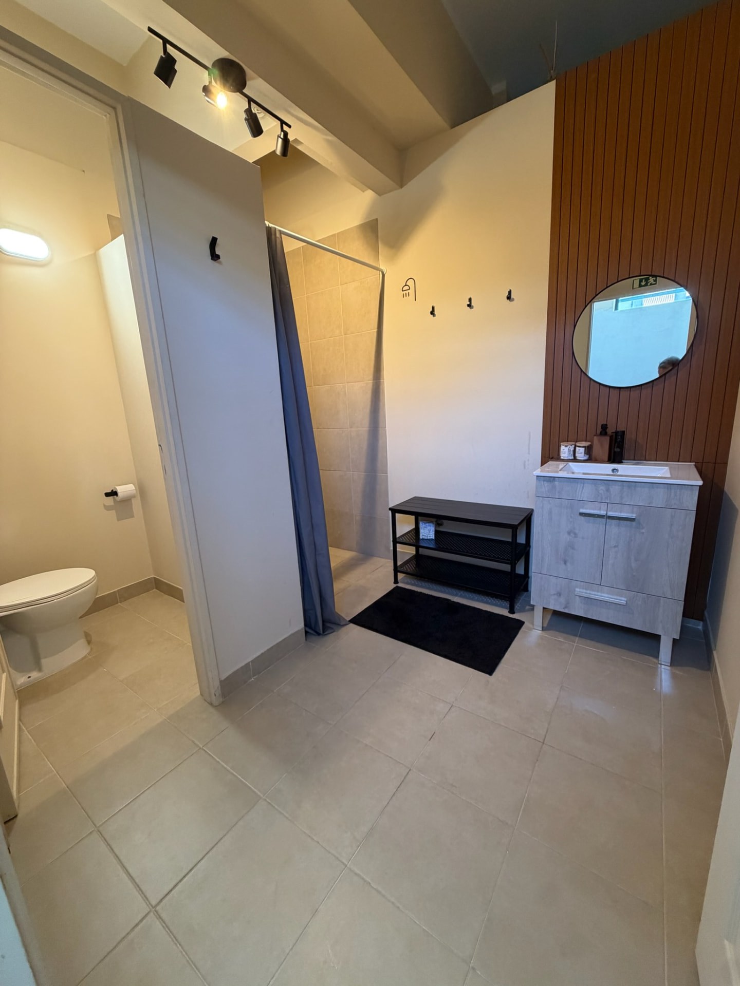 Balneário do estúdio SAL com duche, espelho redondo e móvel de lavabo