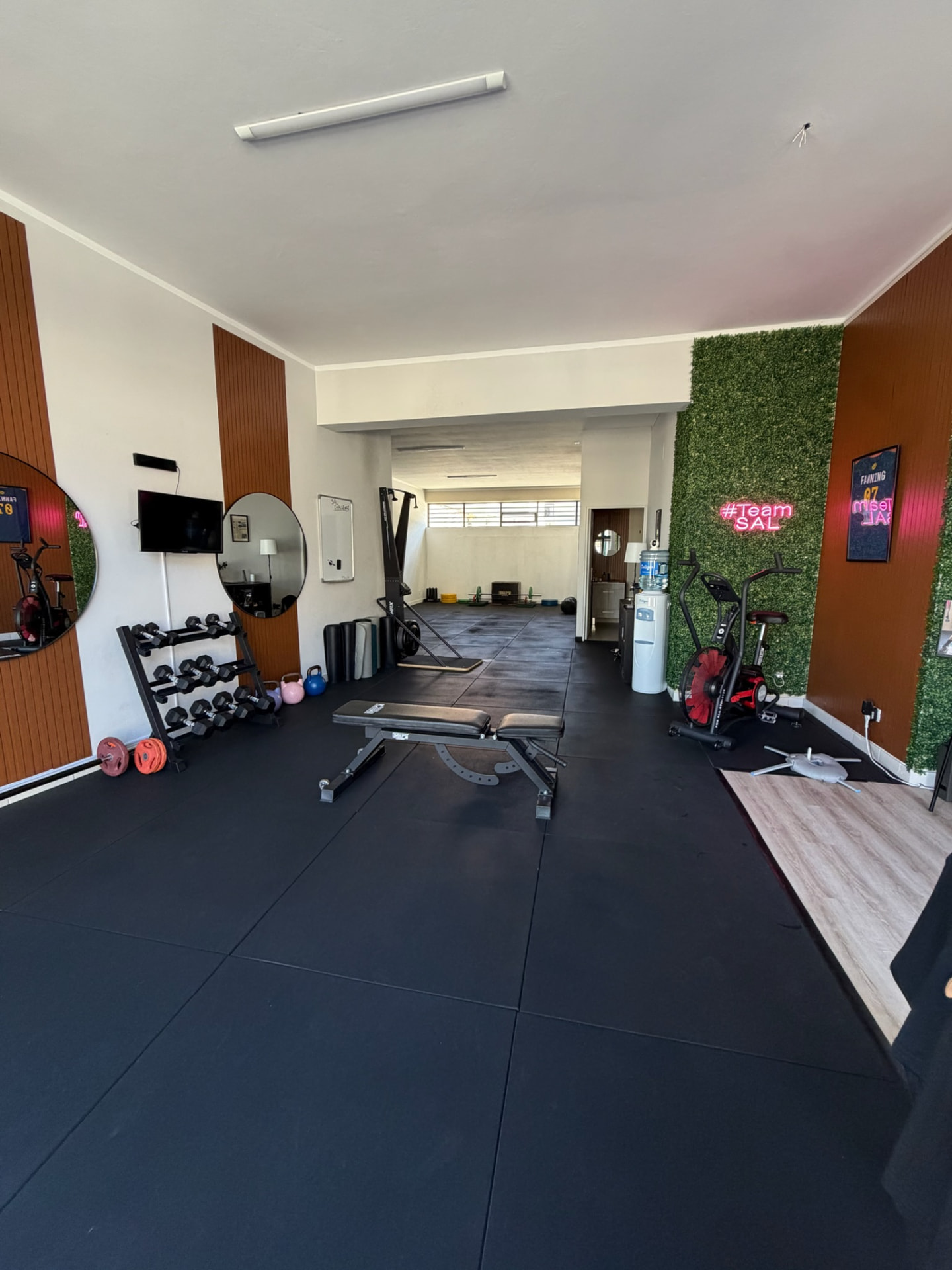 Sala de treino do estúdio SAL Personal Training com banco, halteres e parede verde #TeamSAL