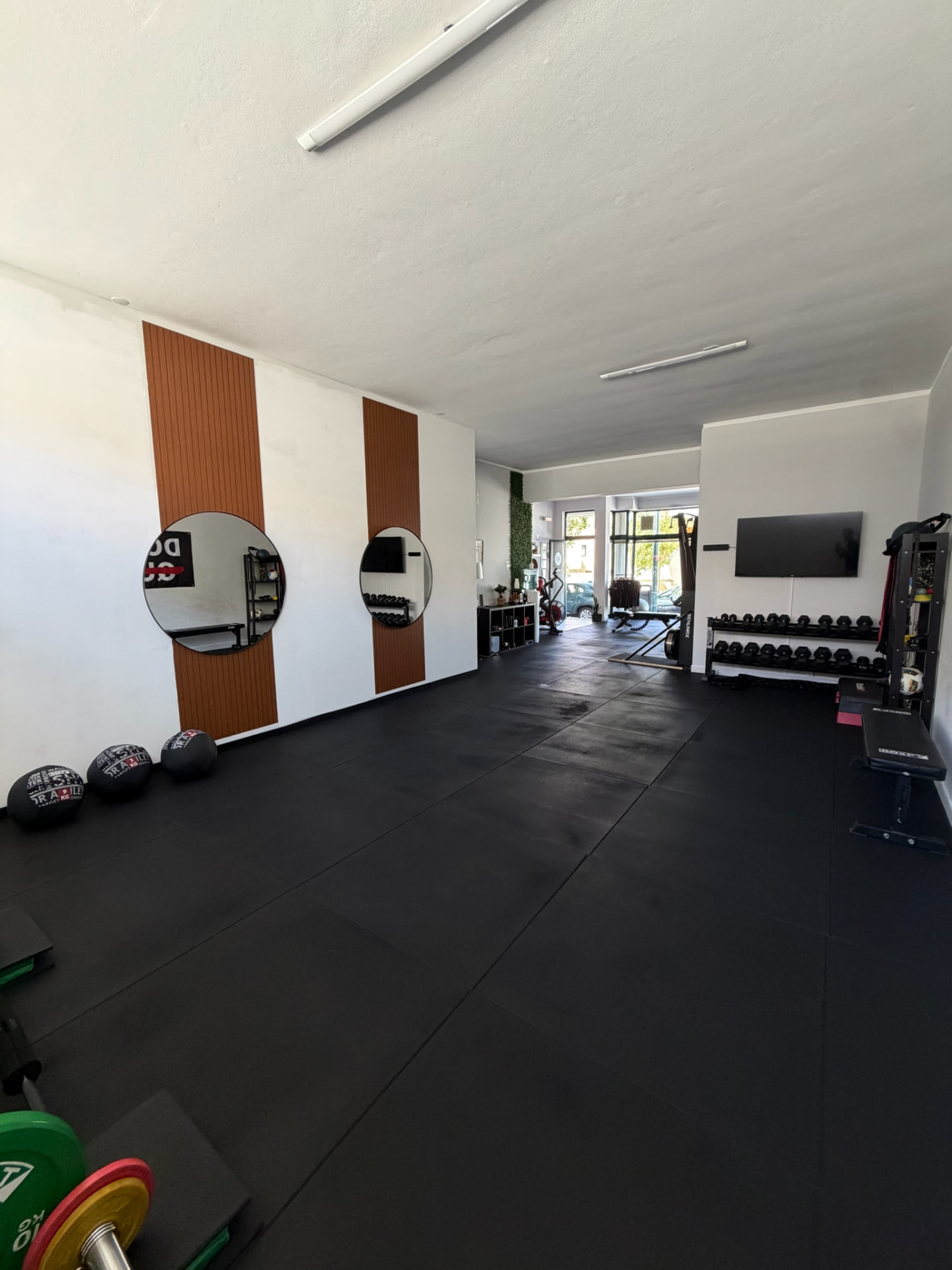 Zona de treino com espelhos redondos, prateleira de halteres e equipamento de força